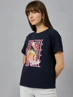 Woman wears 98degreenorth Womens Cotton Typography Graphic Tee – Relaxed Fit, paired with white pants against a gray backdrop.