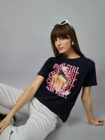Woman in a navy 98degreenorth Women’s Cotton Typography Graphic Tee, white pants, and sunglasses sits on the floor.