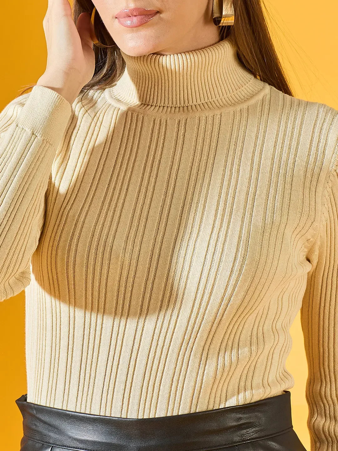 Woman wears 98degreenorth Cream Ribbed Turtleneck Sweater, posing against a yellow background in a black skirt.