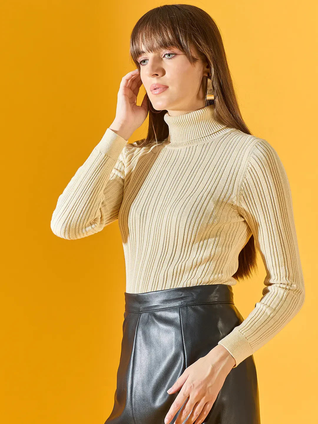 Woman in 98degreenorth’s cream ribbed turtleneck sweater poses against a vibrant yellow background.