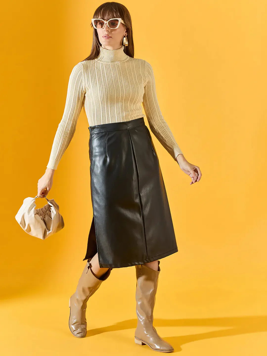 Woman in 98degreenorth cream ribbed turtleneck sweater holds a beige bag, styled with black skirt and tan boots.