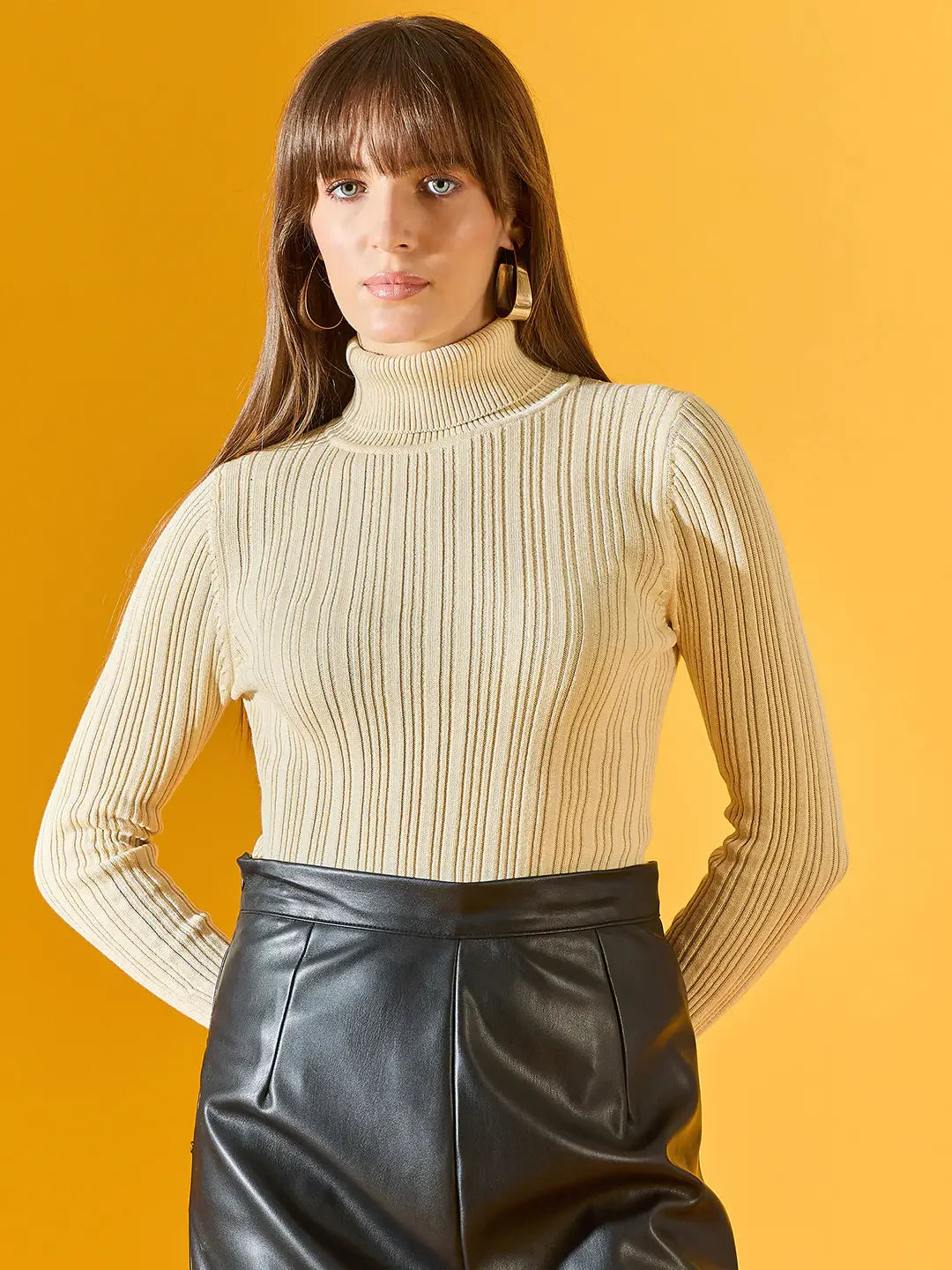 Woman wears 98degreenorth cream ribbed turtleneck sweater and black leather skirt against a yellow background.