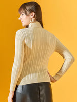 Woman with long brown hair in a 98degreenorth cream ribbed turtleneck sweater and black skirt, on a yellow background.