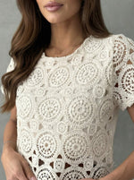 Woman in 98degreenorth Women's Crochet Lace Crop Top—off white, short sleeves, scalloped hem—against a gray background.