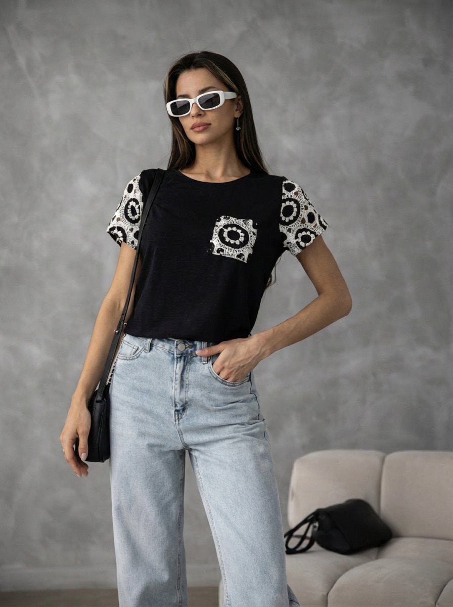 Woman in sunglasses wears 98degreenorth Women's Crochet Sleeve Contrast Top - Black with light jeans, hand in pocket.