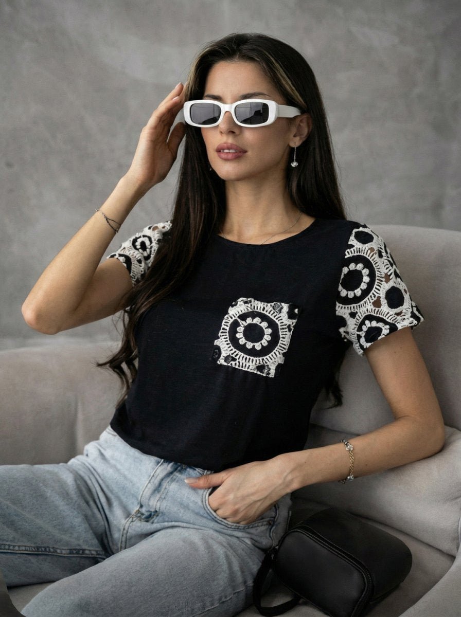 Woman in white sunglasses, light jeans, and a 98degreenorth Crochet Sleeve Contrast Top sitting on a light chair.