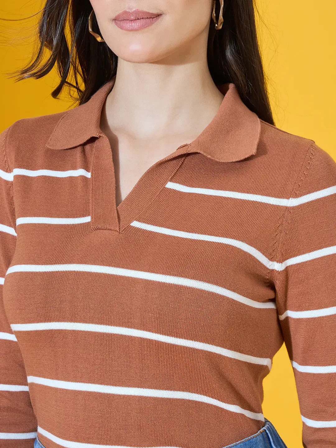 A woman in a 98degreenorth Dark Camel Striped Collared Sweater stands against a bright yellow background.