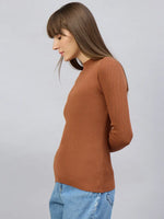 Woman wears 98degreenorth Dark Camel Turtle Neck Ribbed Sweater with blue jeans, standing sideways against a light background.