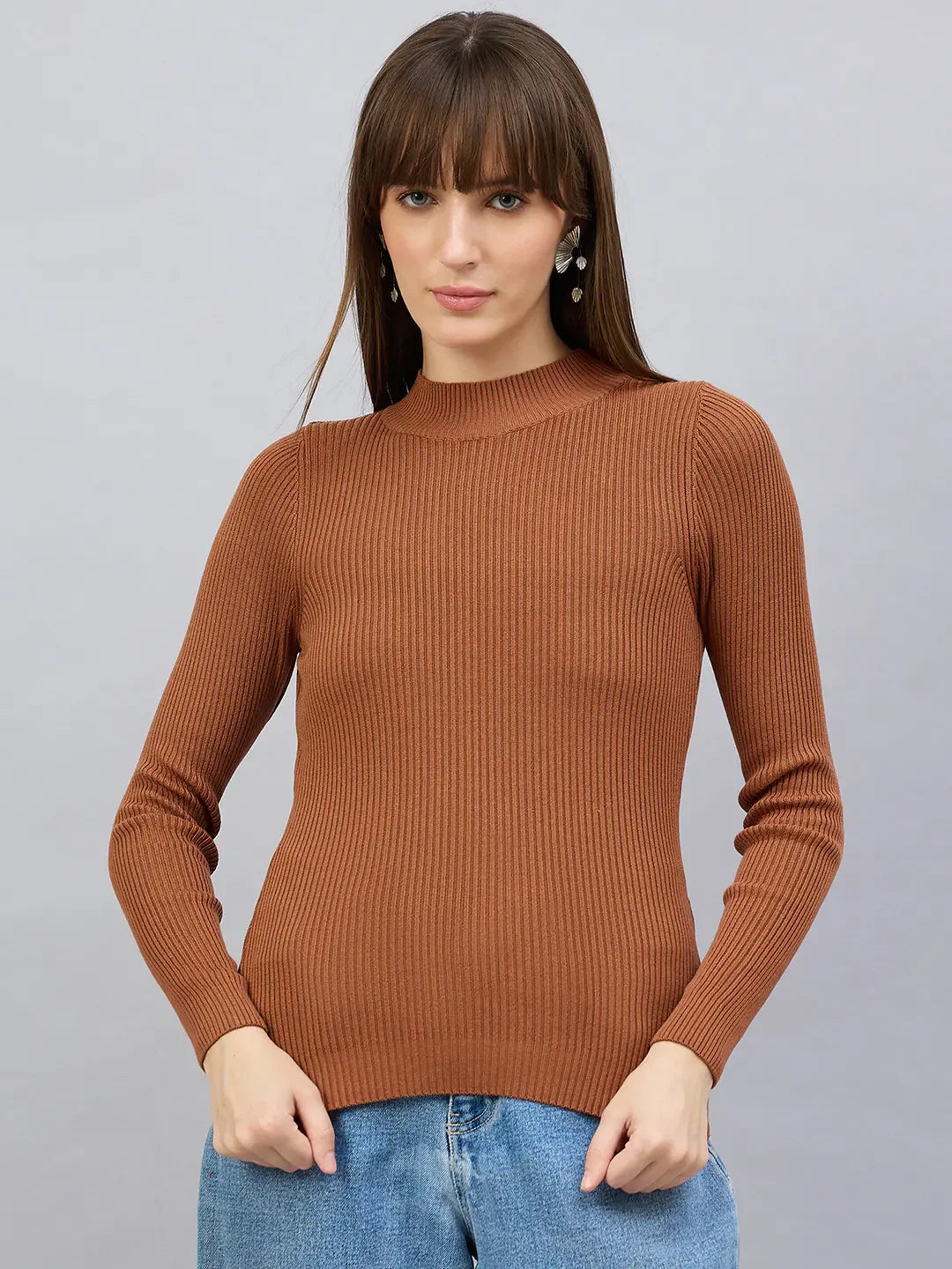 Woman wears 98degreenorth Women’s Dark Camel Turtle Neck Ribbed Sweater with blue jeans against a grey background.
