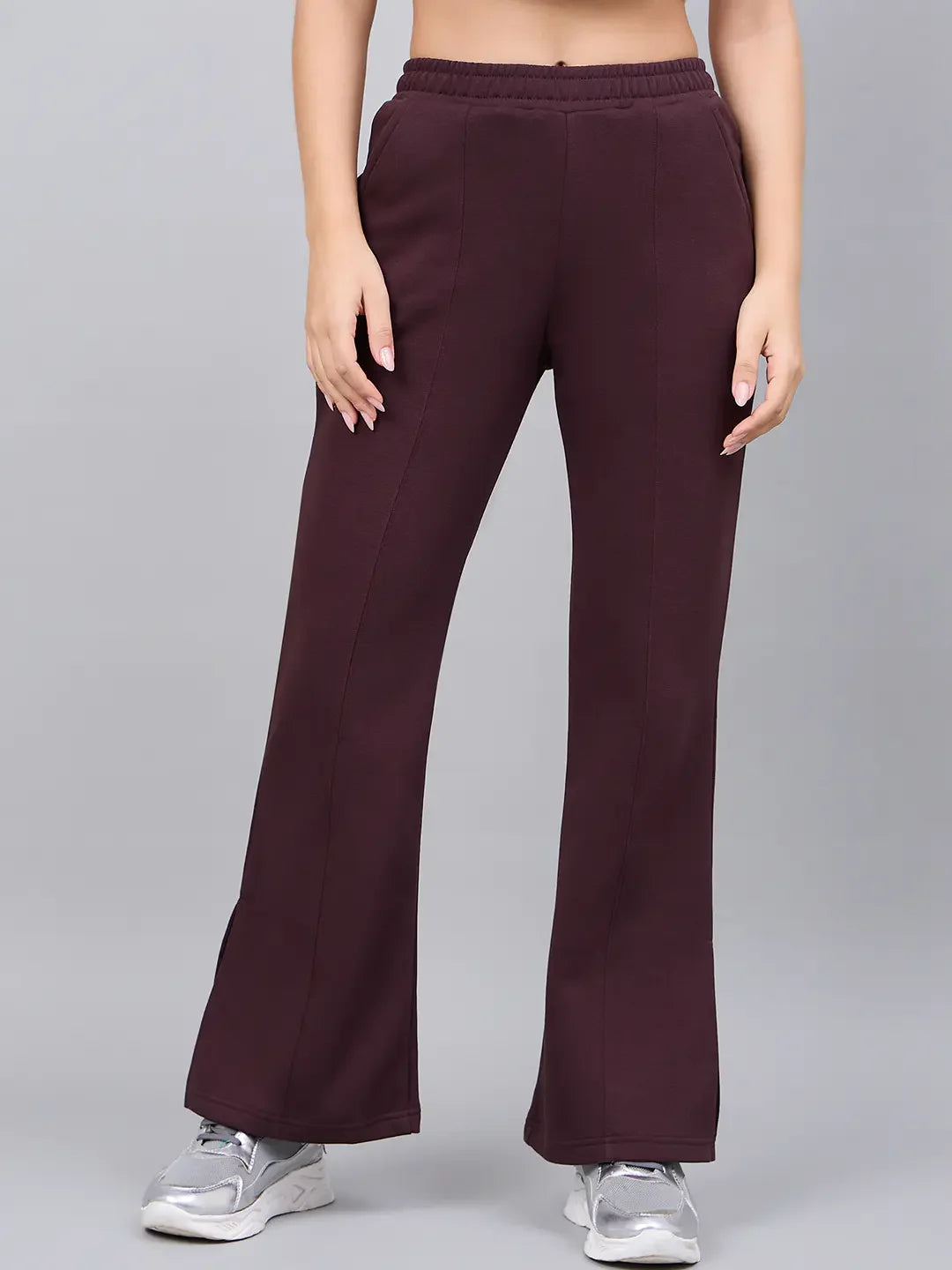 A woman models 98degreenorth’s Dark Wine Bootcut Sweatpants with side slit, standing against a gray backdrop.
