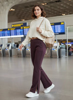 A woman in 98degreenorth Dark Wine Bootcut Sweatpants with side slit walks through an airport terminal with flight boards.