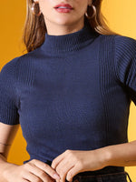 Woman wearing a 98degreenorth denim blue ribbed turtle neck sweater, slim fit, against a yellow background.