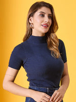 Woman with wavy brown hair in a 98degreenorth denim blue ribbed turtle neck slim fit sweater, against a yellow background.