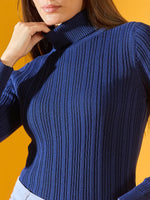 Woman in 98degreenorth denim blue ribbed slim fit turtleneck sweater, cozy winter wear, on a yellow background.