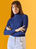 Woman wears 98degreenorth’s denim blue ribbed turtleneck sweater with light jeans, standing against a yellow background.