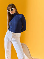 Woman models 98degreenorth's denim blue slim fit ribbed turtleneck sweater against a bright yellow background.