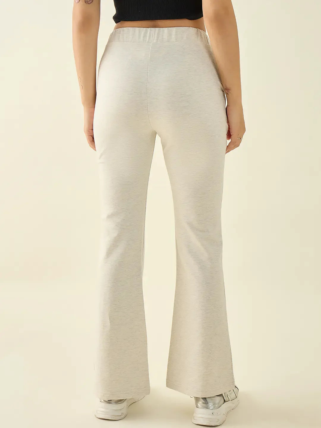 A person wears 98degreenorth Women’s Ecru Flared Bootcut Trousers, white sneakers, and a black top, shown from the back.