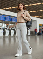 Woman in ecru 98degreenorth flared bootcut sweatpants stands at airport with black backpack near check-in kiosks.