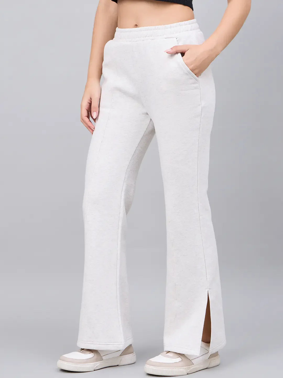 Someone in 98degreenorth’s ecru flared bootcut side-slit lounge pants, white sneakers, and a black top.