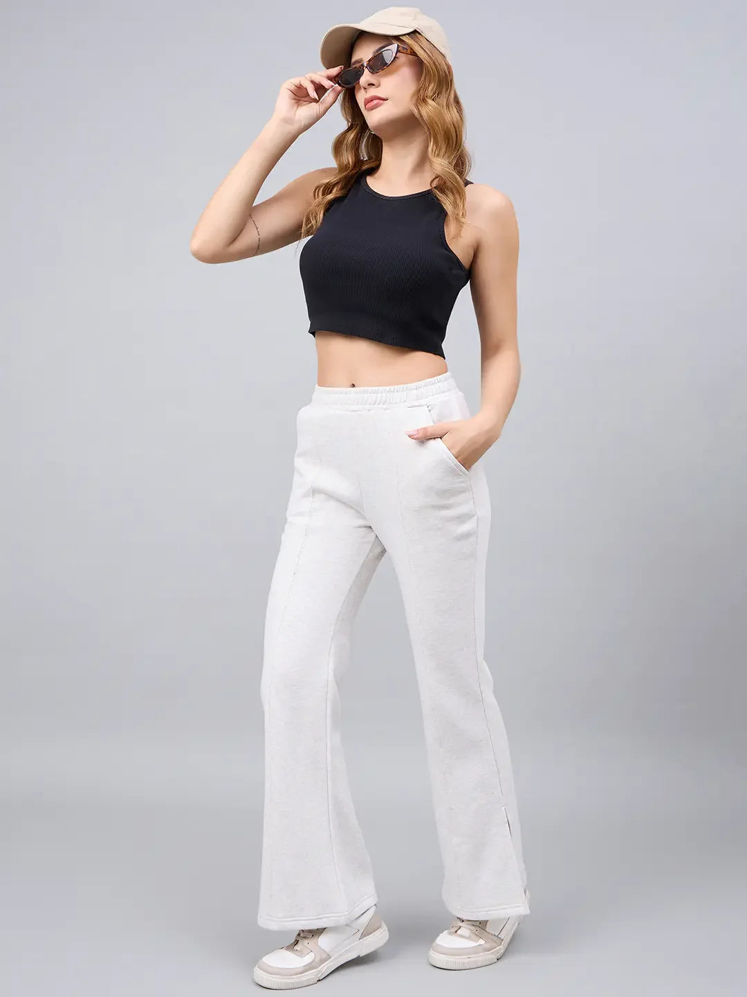 Woman in a black crop top, 98degreenorth ecru flared bootcut sweatpants, sneakers, beige cap, and sunglasses.