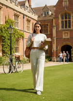 A student in 98degreenorth Women’s Ecru Flared Fit Bootcut Cotton Trousers walks on campus with books.