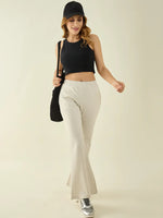 Woman in a black crop top and 98degreenorth ecru flared cotton trousers, with a cap, silver sneakers, and a shoulder bag.
