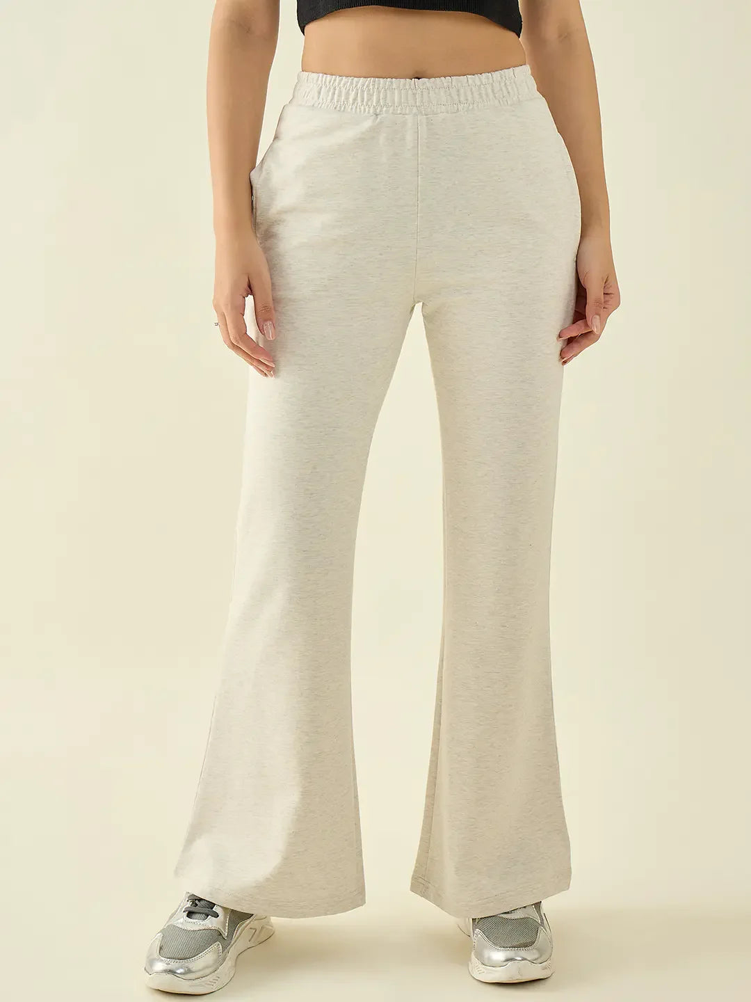 Person in 98degreenorth Ecru Flared Bootcut Trousers, silver sneakers, black crop top, against a plain background.