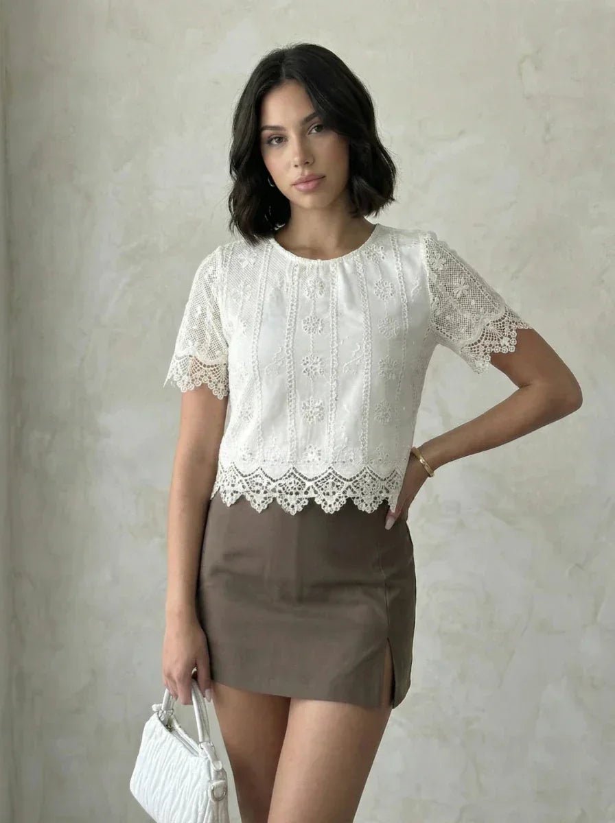Woman in 98degreenorth Beige Embroidered Lace Crop Top with scalloped hem and taupe mini skirt, holding white purse.