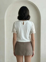 A woman with short dark hair wears a 98degreenorth beige embroidered lace crop top with scalloped hem and short sleeves.