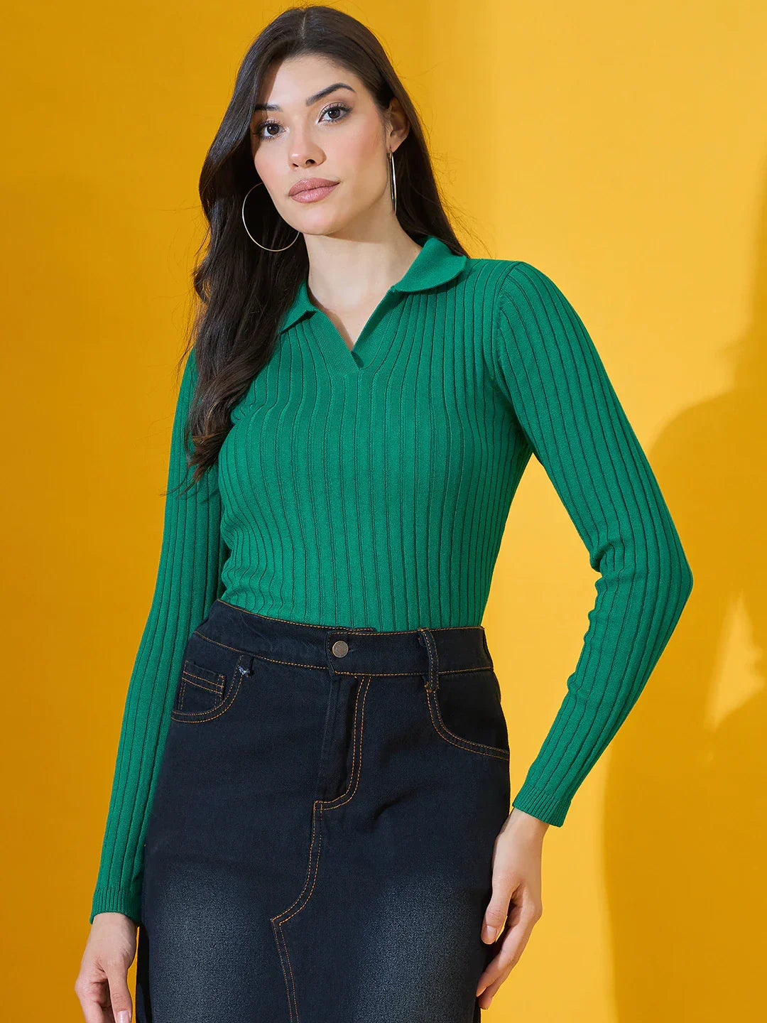 Model wears 98degreenorth Women’s Emerald Green Ribbed Collar Neck Sweater with a dark denim skirt against yellow.