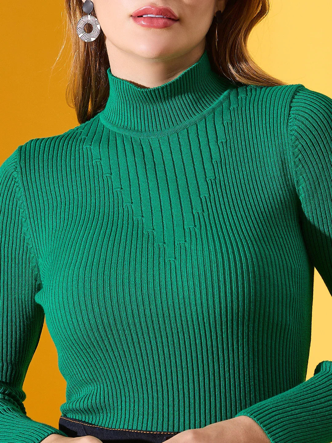 A woman wears a 98degreenorth emerald green ribbed turtle neck sweater and large earrings on a yellow background.