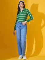 A woman wears a 98degreenorth fern green striped collared sweater with blue jeans and white sneakers against a yellow background.