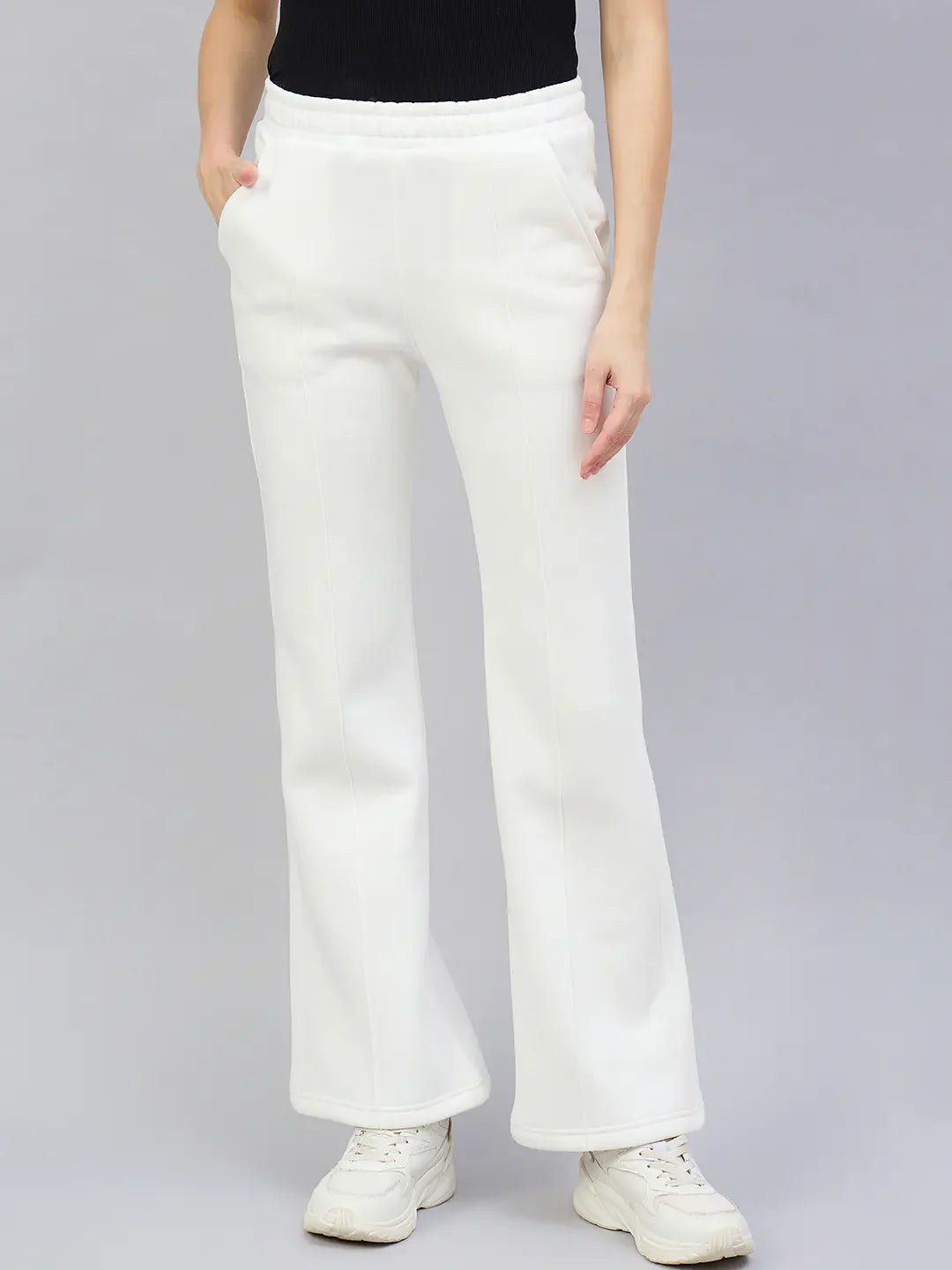 Model wears 98degreenorth Women’s Flared Bootcut Fleece Sweatpants in Off White with white sneakers and a black top.