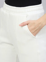 A person wears 98degreenorth Women’s Flared Bootcut Fleece Sweatpants in Off White, hand in pocket, waist-down view.