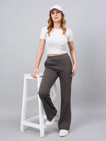 Woman in 98degreenorth Women’s Olive Flared Bootcut Fleece Sweatpants stands by a white stool on a gray background.