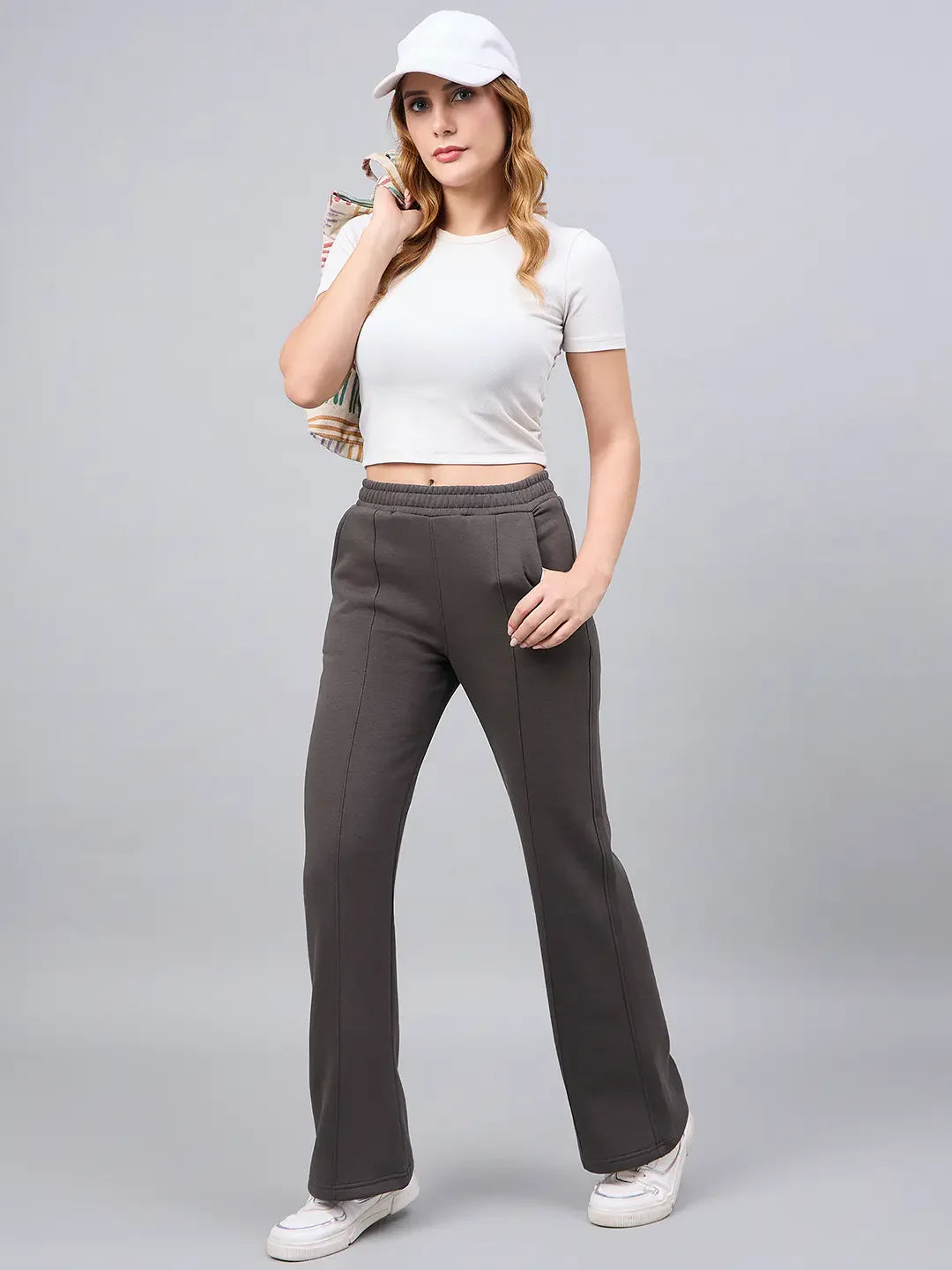 Woman wears 98degreenorth’s olive flared bootcut fleece sweatpants, white crop top, and cap against a gray background.