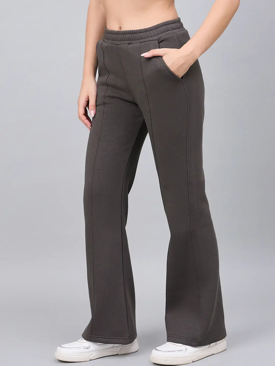 A woman in 98degreenorth olive flared bootcut fleece sweatpants stands casually with white sneakers against a gray background.