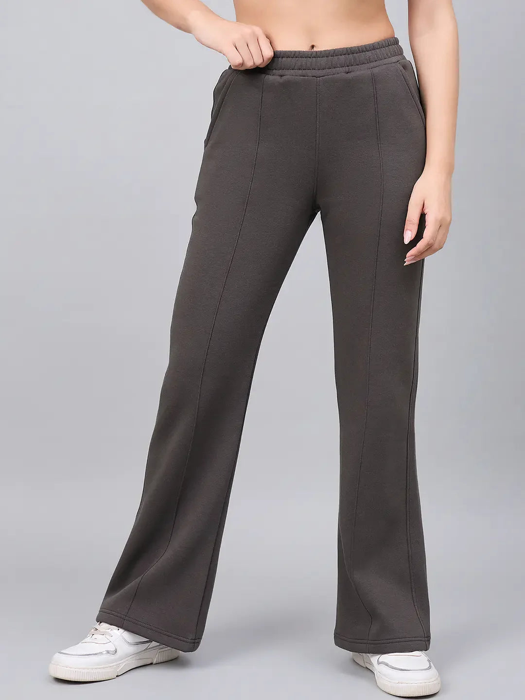 Model in 98degreenorth Women’s Flared Bootcut Fleece Sweatpants in Olive, white sneakers, and a grey backdrop.