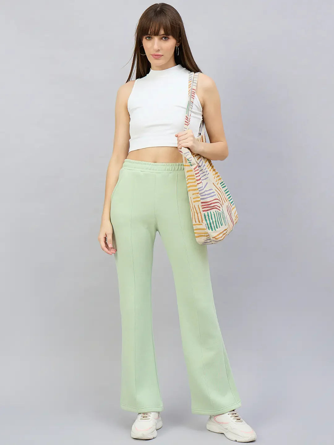 Woman in a white crop top, 98degreenorth pista flared fleece sweatpants, white sneakers, with a colorful shoulder bag.