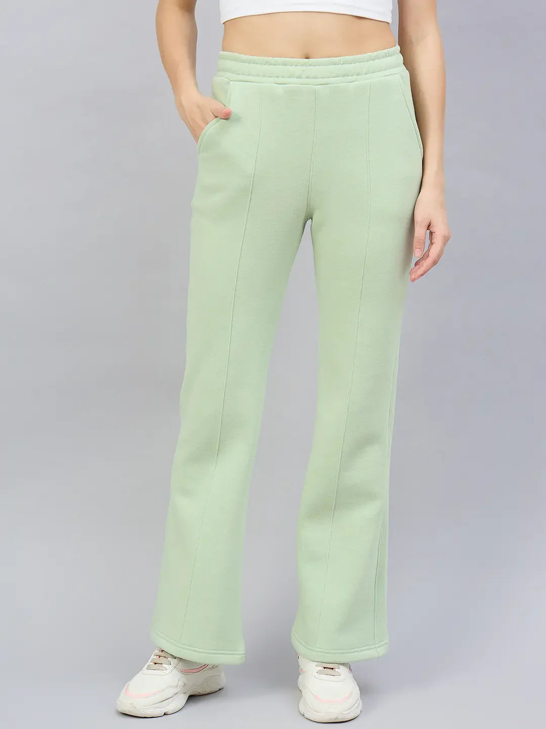 Woman in 98degreenorth’s Pista Flared Fleece Sweatpants, white crop top, and sneakers on a plain gray background.