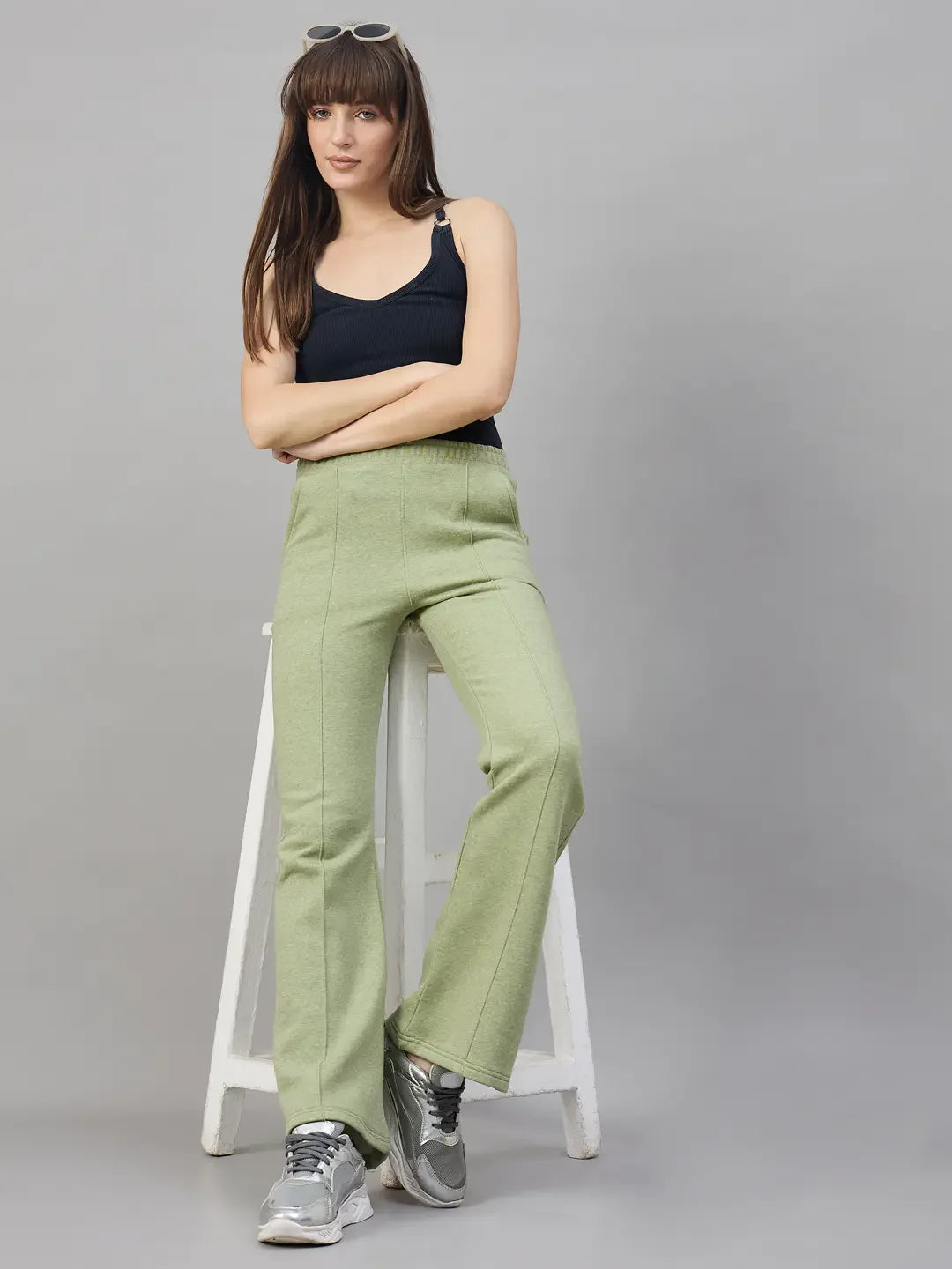 Woman wears 98degreenorth Women’s Flared Bootcut Fleece Sweatpants in Pista Melange, seated against a gray backdrop.