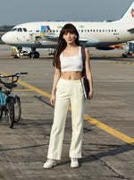 Woman in 98degreenorth Butter Yellow Flared Sweatpants stands on an airport tarmac with a bike and plane behind her.