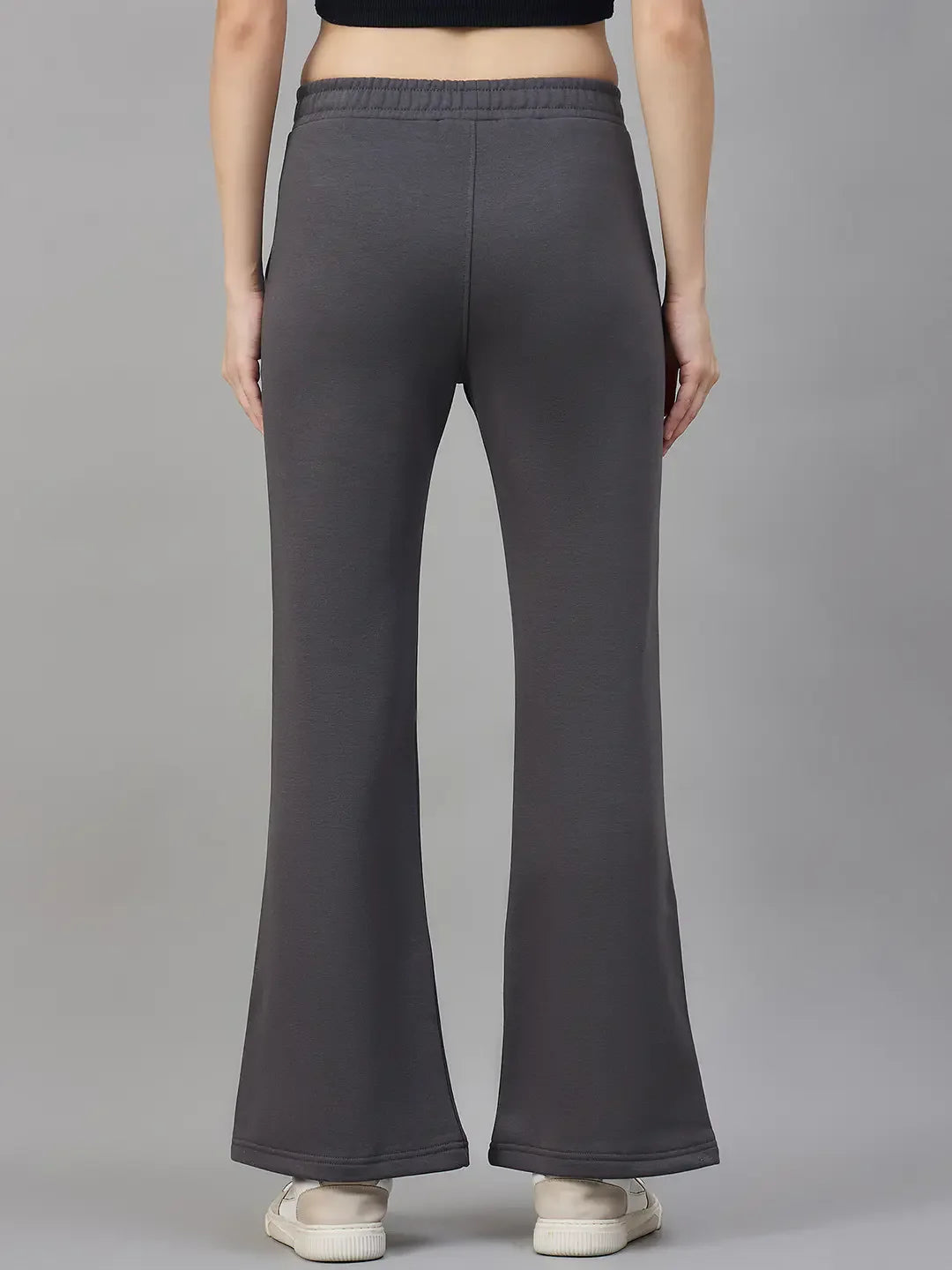 Model wears 98degreenorth Women’s Flared Sweatpants in Charcoal Grey fleece and white sneakers, shown from the back.