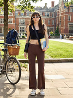 A young woman in 98degreenorth Women’s Flared Sweatpants in Cocoa Brown stands by her bike with books near campus.
