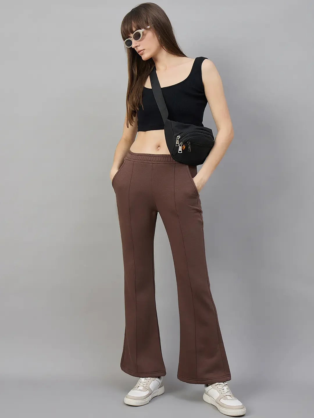 Woman in 98degreenorth Women’s Flared Sweatpants in Cocoa Brown, crop top, sneakers, sunglasses, and a crossbody bag.
