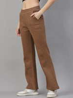 A woman wears 98degreenorth Women’s Flared Sweatpants in Coffee Melange with pockets and white sneakers, on grey background.