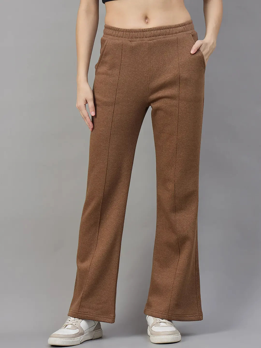 Model wearing 98degreenorth Women’s Flared Sweatpants in Coffee Melange, posing with one hand in pocket against gray.