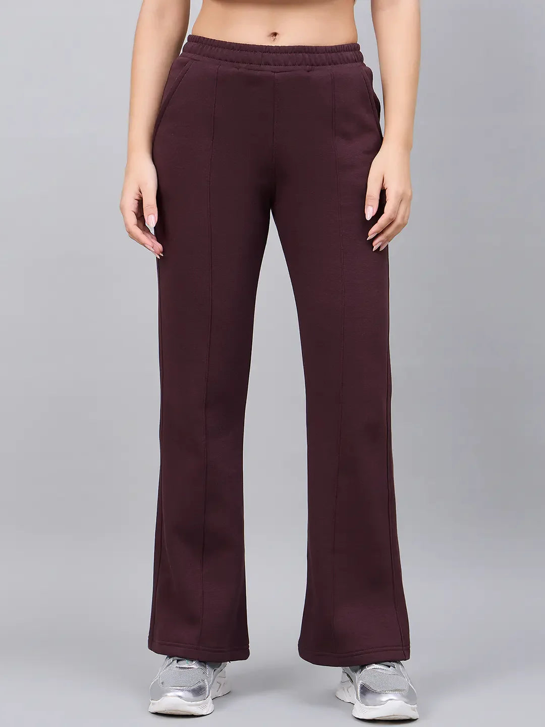 Model in 98degreenorth Women’s Flared Sweatpants in Dark Wine and silver sneakers, poses against a plain gray backdrop.