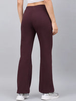 Model in 98degreenorth Women’s Flared Sweatpants in Dark Wine, white sneakers, and crop top, back view on grey.