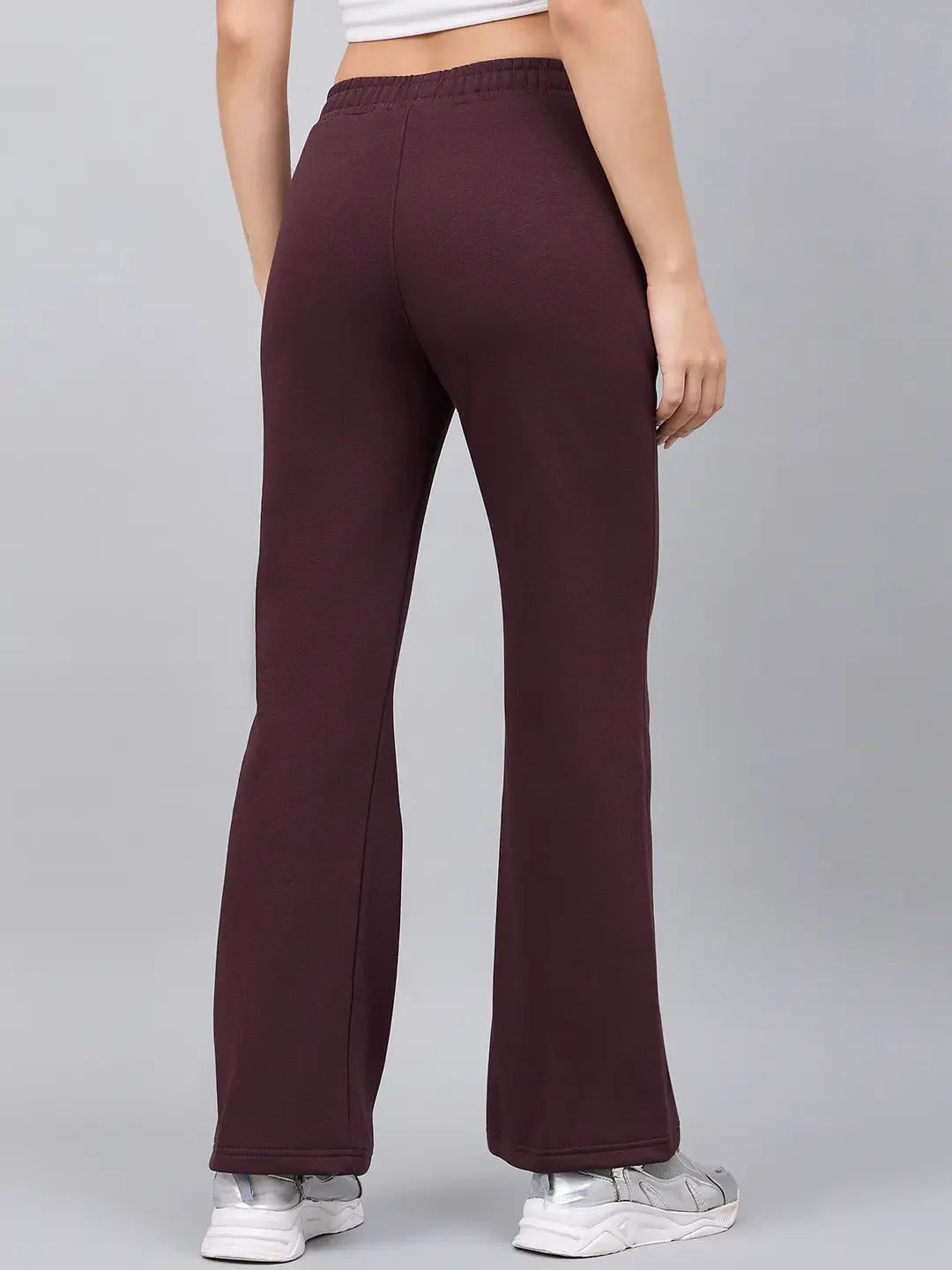 Model in 98degreenorth Women’s Flared Sweatpants in Dark Wine, white sneakers, and crop top, back view on grey.